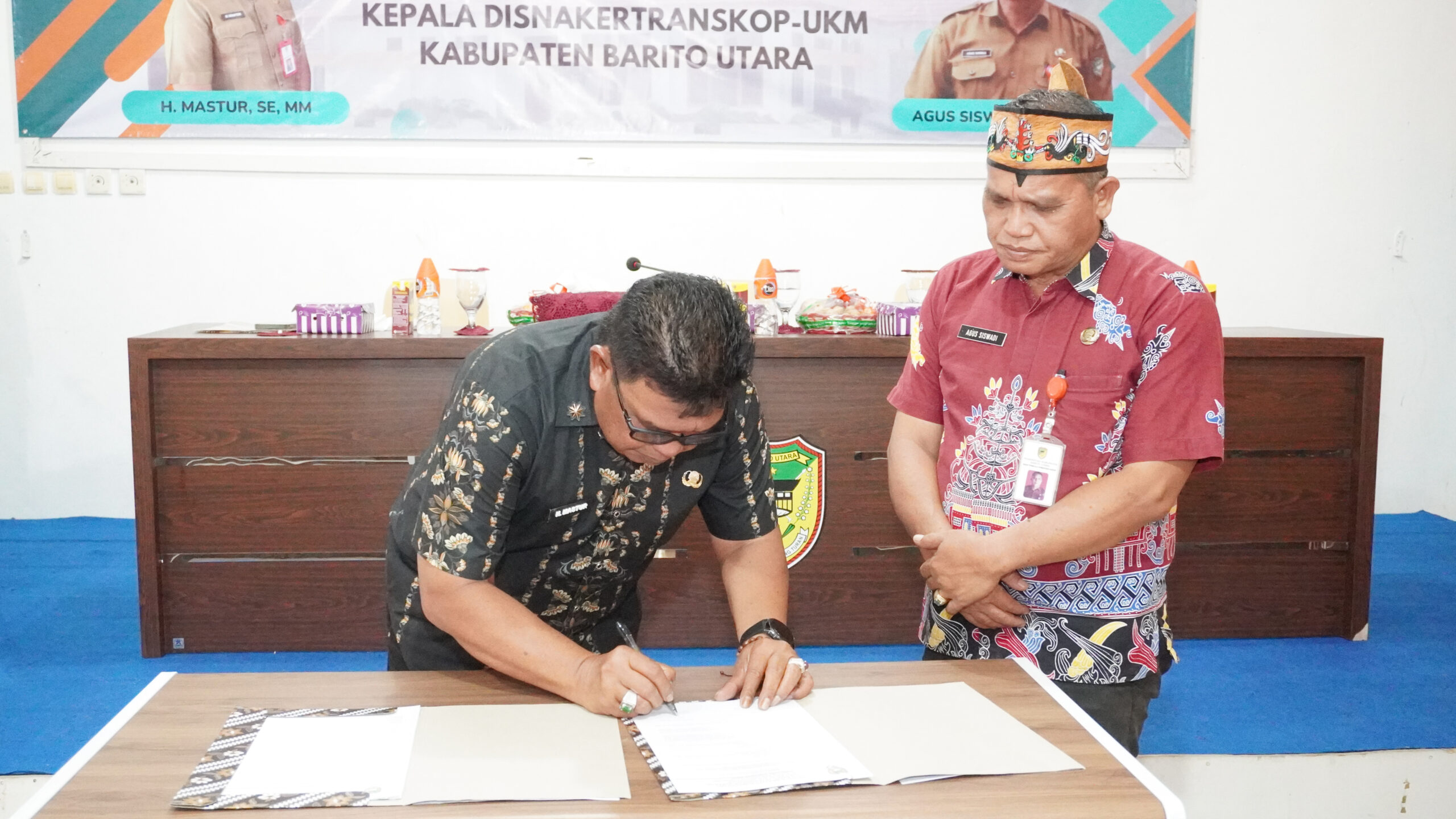 H. Mastur, S.E., M.M menandatangani berita acara serah terima jabatan Kepala Disnakertranskop UKM Kabupaten Barito Utara disaksikan Agus Siswadi, S.Pt., M.IP di Aula Disnakertranskop UKM Barito Utara, Jumat, 8 Mei 2026.